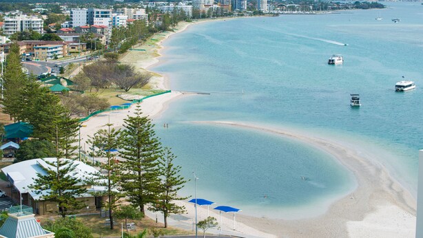 Un paysage urbain côtier avec une plage, une eau d’un bleu limpide et plusieurs immeubles de grande hauteur en arrière-plan.