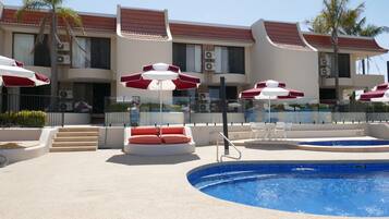 A pool area with red and white umbrellas, lounge chairs, and a clear blue pool.