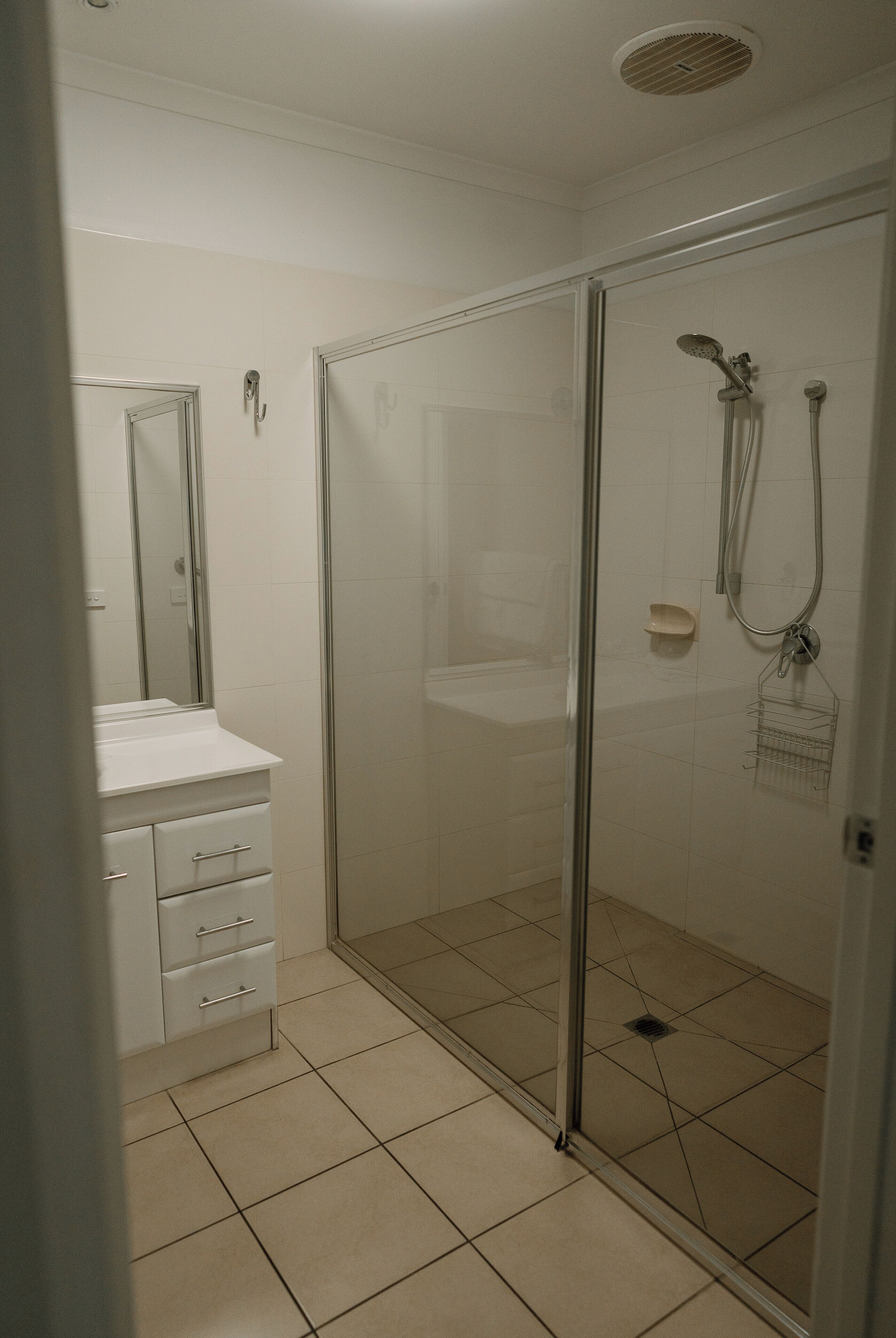 Un bagno con doccia vetrata, lavandino bianco con specchio e pavimento piastrellato.