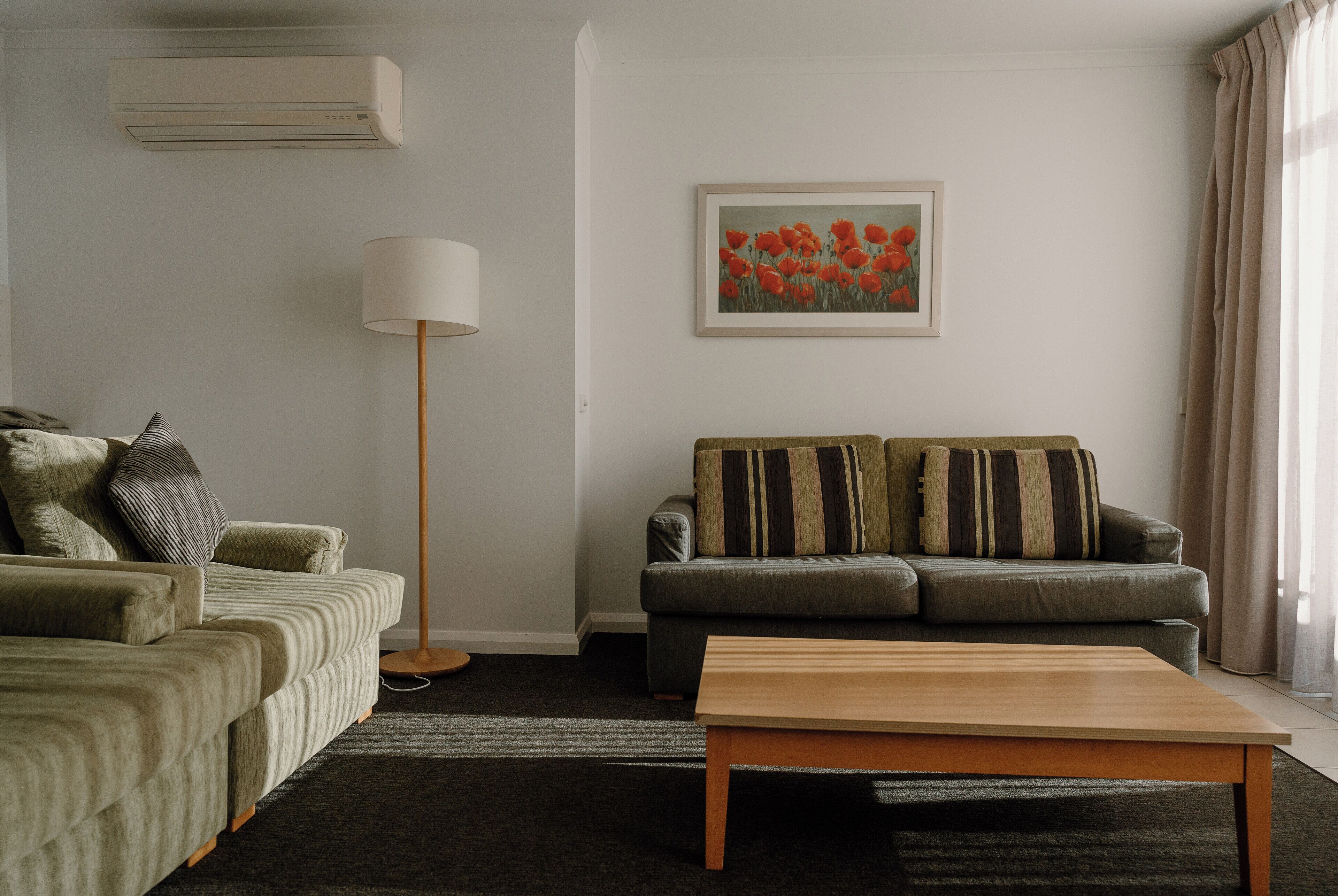 A living room with a sofa, a floor lamp, a painting, and a window with curtains.