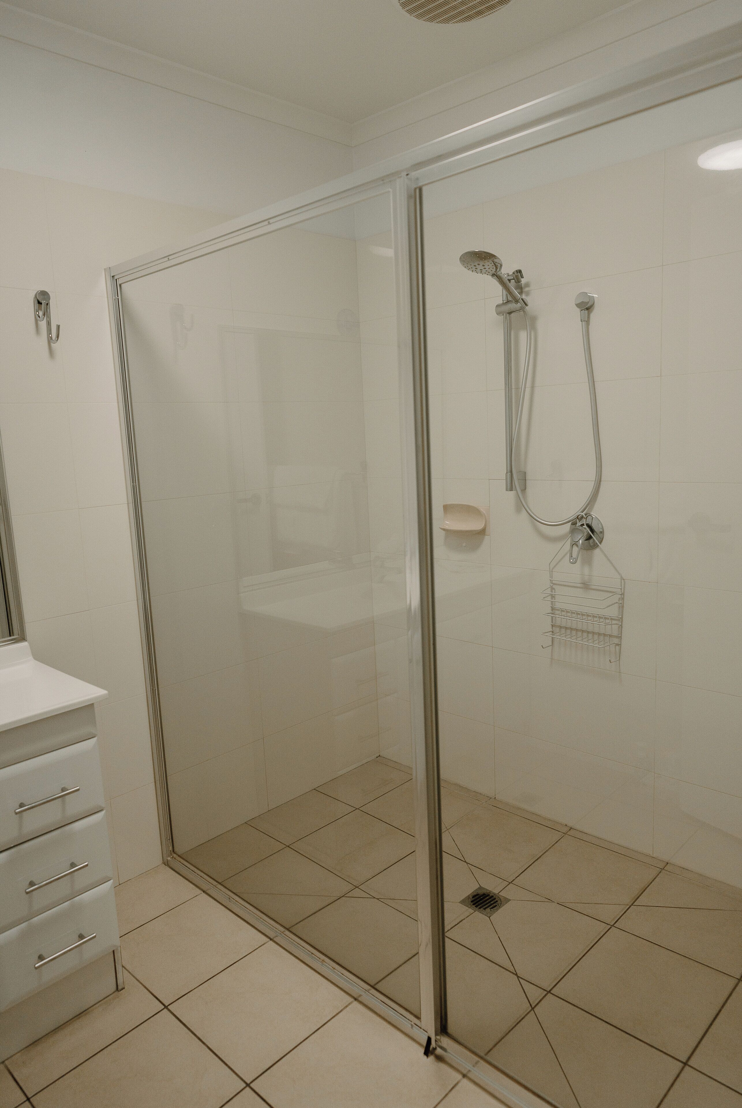 A glass-enclosed shower area with a handheld showerhead and a handheld faucet.