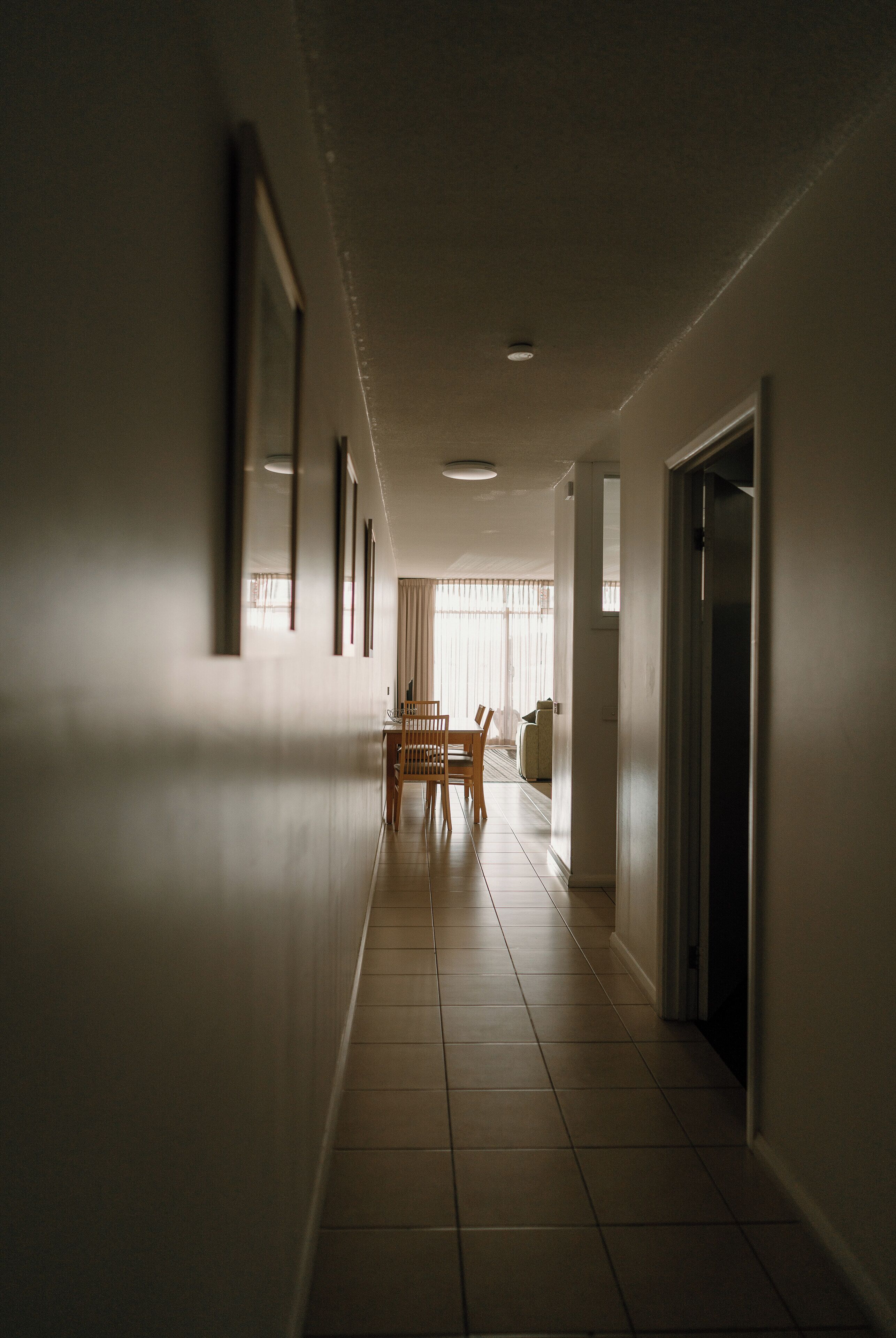 A hallway with a dining area at the end, featuring a table and chairs.