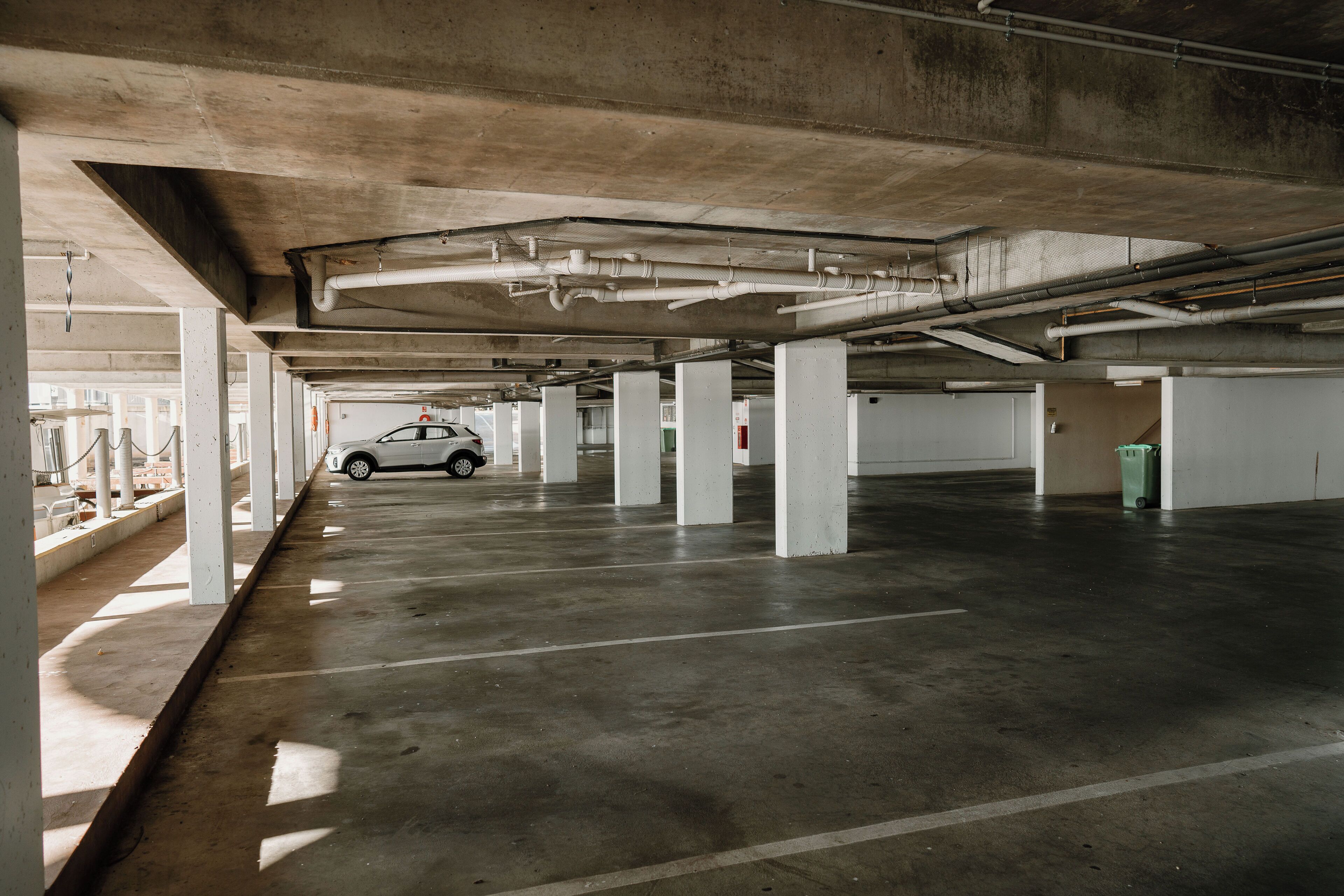 An underground parking garage with concrete pillars and a white car parked in the distance.