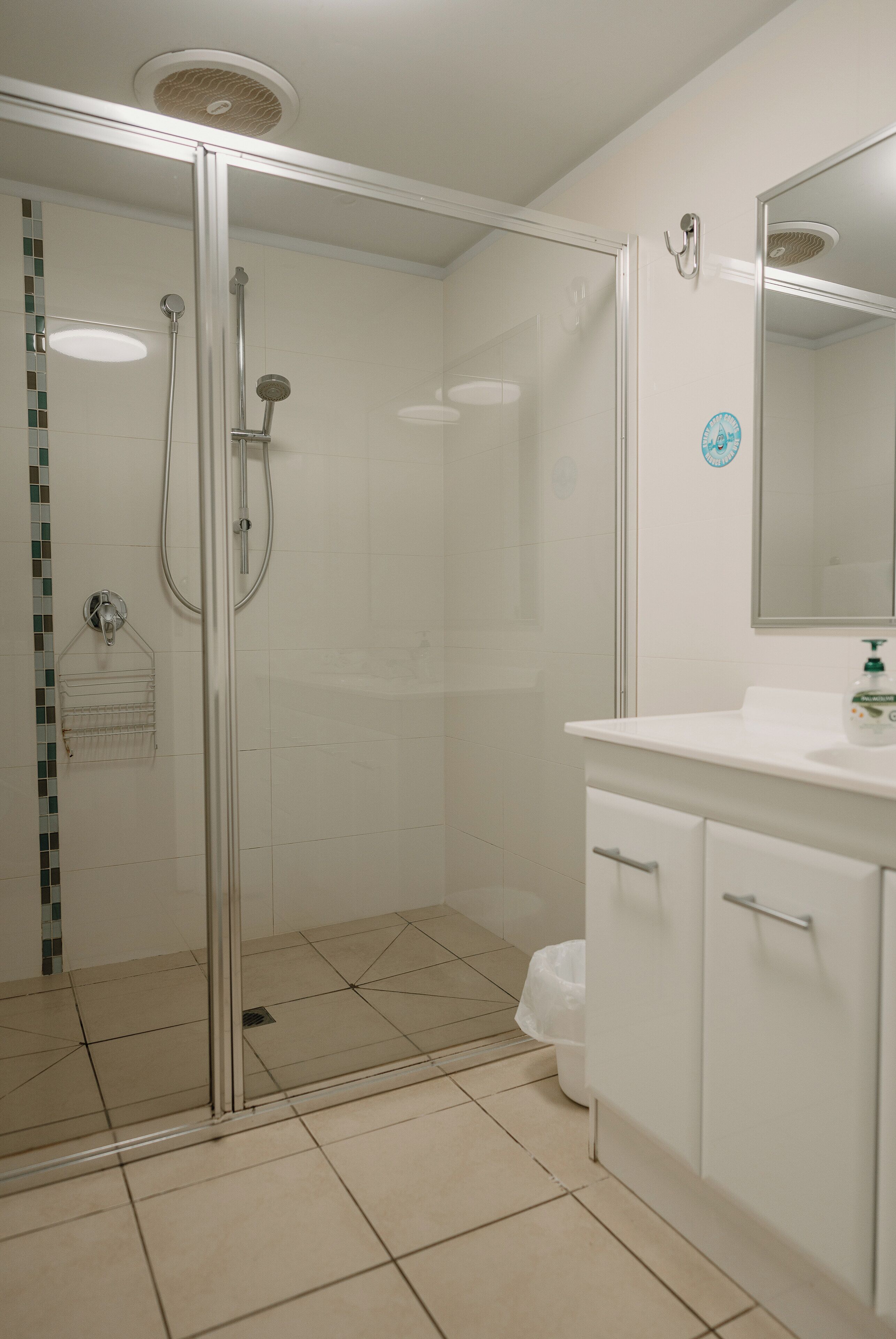 A modern bathroom with a glass-enclosed shower, a white sink with a mirror, and a tiled floor.