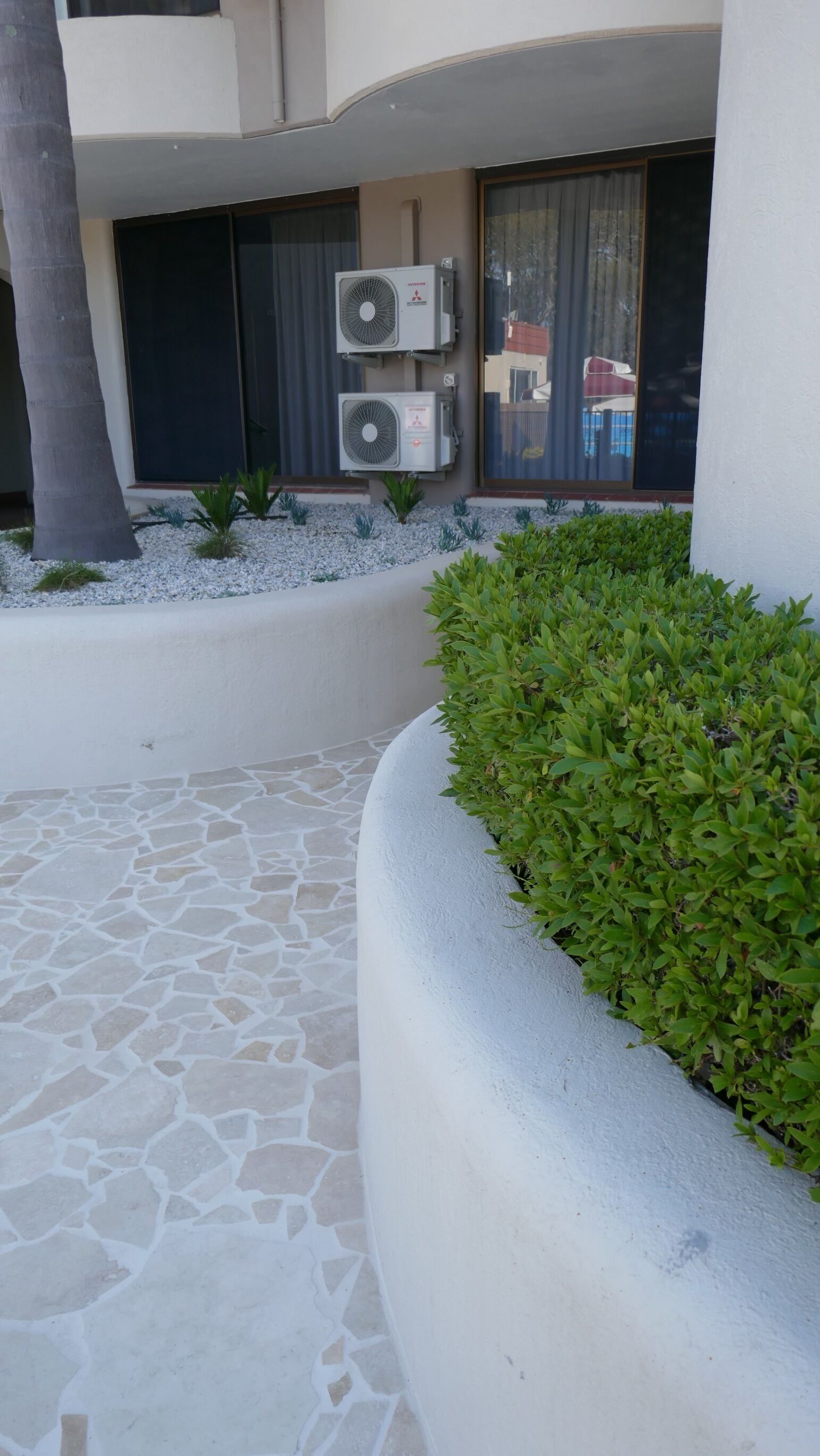 A courtyard with a stone floor, a palm tree, and two air conditioning units mounted on the wall.