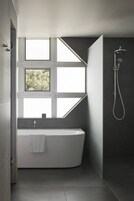 Un baño moderno con una bañera independiente, un cabezal de ducha y una ventana que proporciona luz natural.