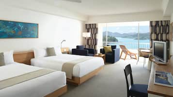 A hotel room with two beds, a desk with a TV, a chair, and a view of the sea.