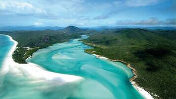 An aerial view of a coastal landscape with a turquoise bay, white sandy beaches, and lush green hills.