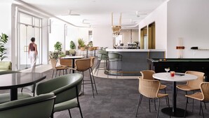 A modern indoor space with round tables and chairs, a pool table, and a bar area.