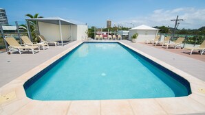 Una piscina rettangolare con bordo piastrellato, circondata da poltrone a sdraio e aree relax con divani.