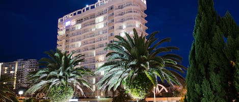 A multi-story hotel with balconies, palm trees, and a parking area.