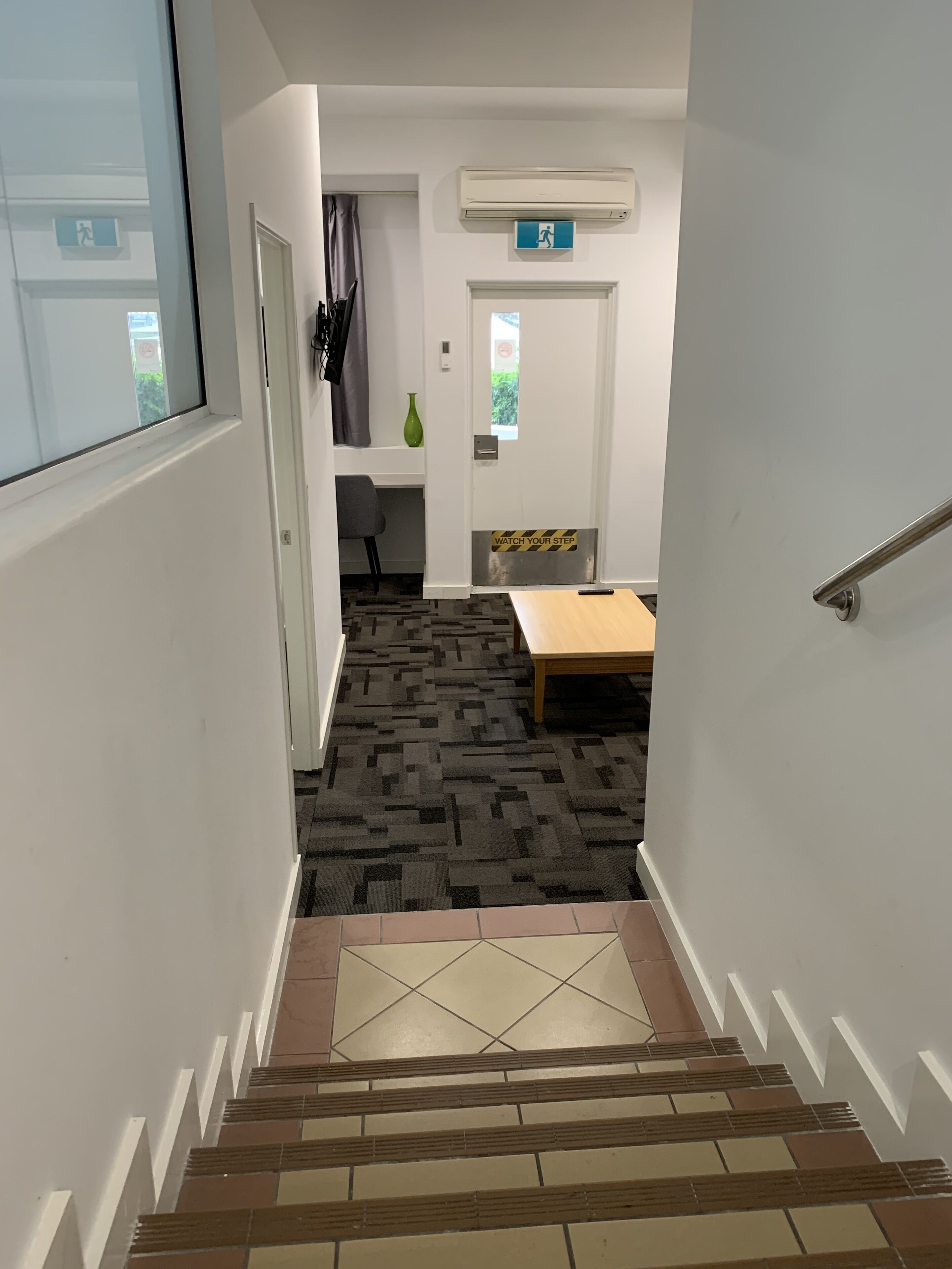 Una escalera con alfombra estampada que lleva a una habitación con cama, una mesa y una silla.