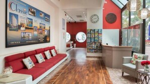 Un'hall d'albergo con un divano rosso, una reception, un grande poster e una sveglia appesa al muro.