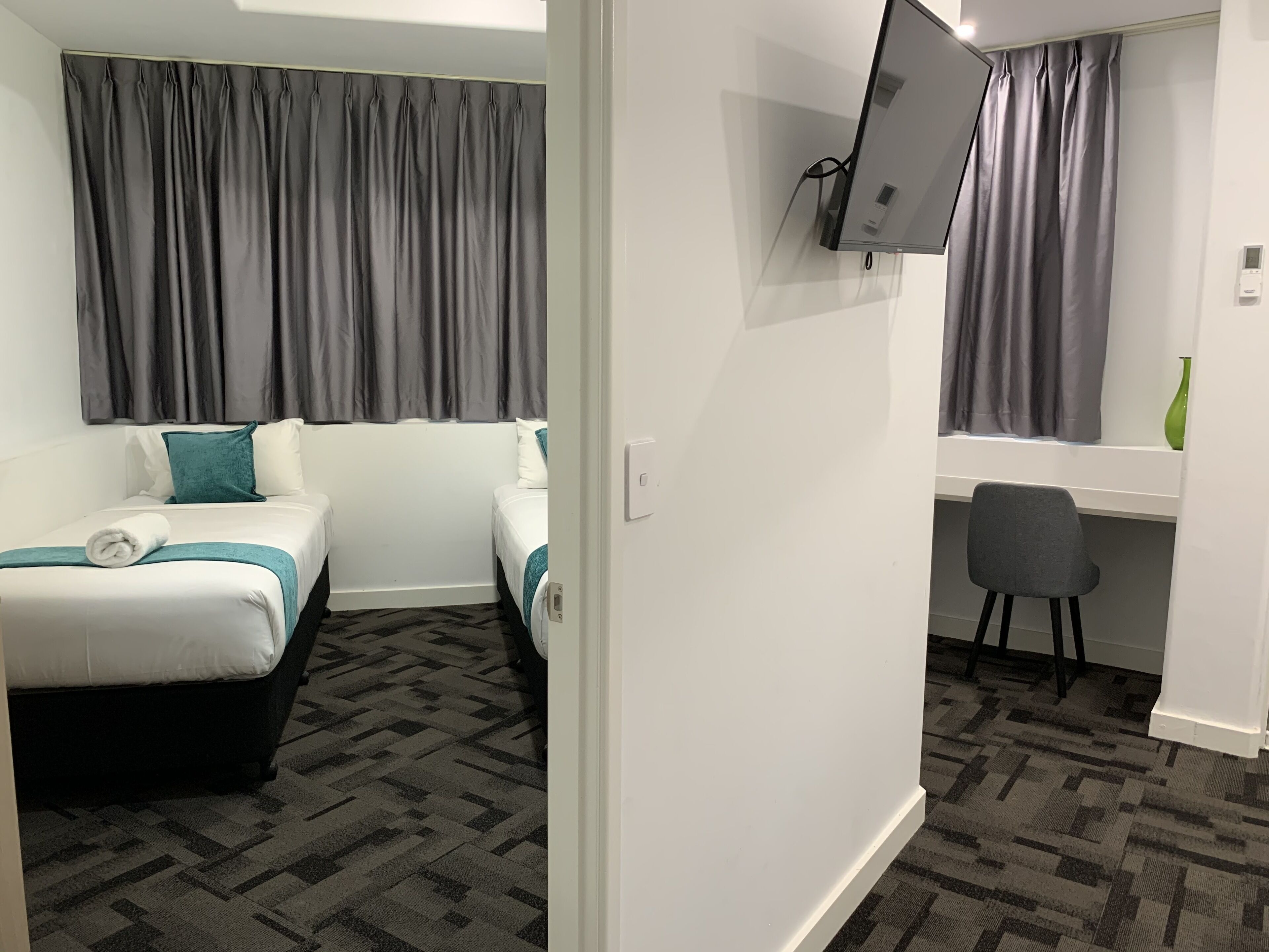 A hotel room with two beds, a desk, a chair, a TV, and a window with curtains.