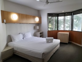 A hotel room with a bed, bedside table, lamp, and a window with a view of trees.