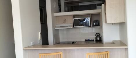A compact kitchen with a microwave, stove, and cabinets. There are two wooden chairs with red cushions.