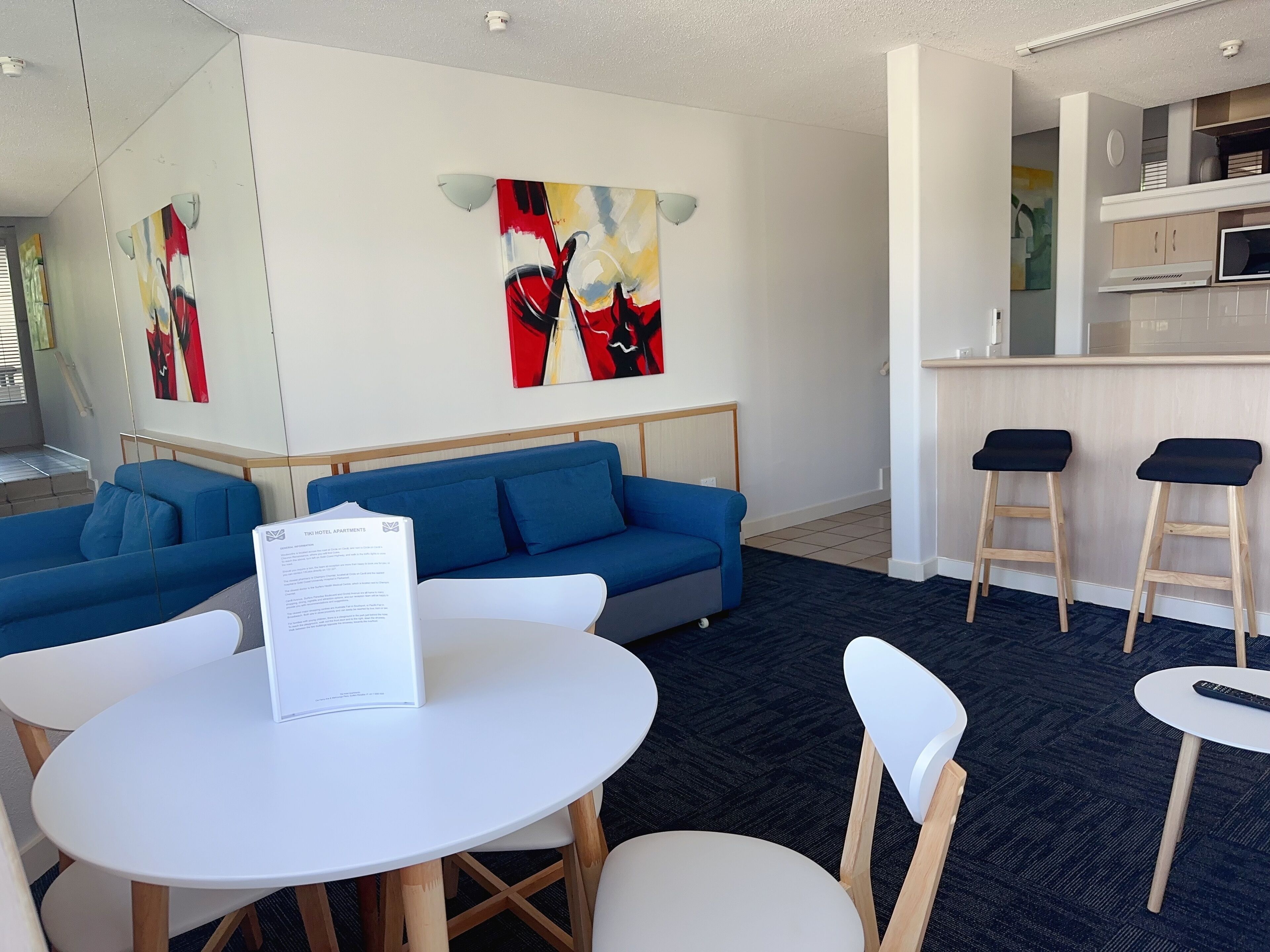 Une chambre d’hôtel moderne avec un canapé bleu, une table ronde blanche et deux tabourets de bar.