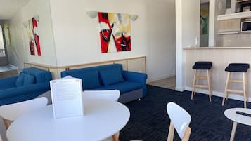 Une chambre d’hôtel moderne avec un canapé bleu, une table ronde blanche et deux tabourets de bar.