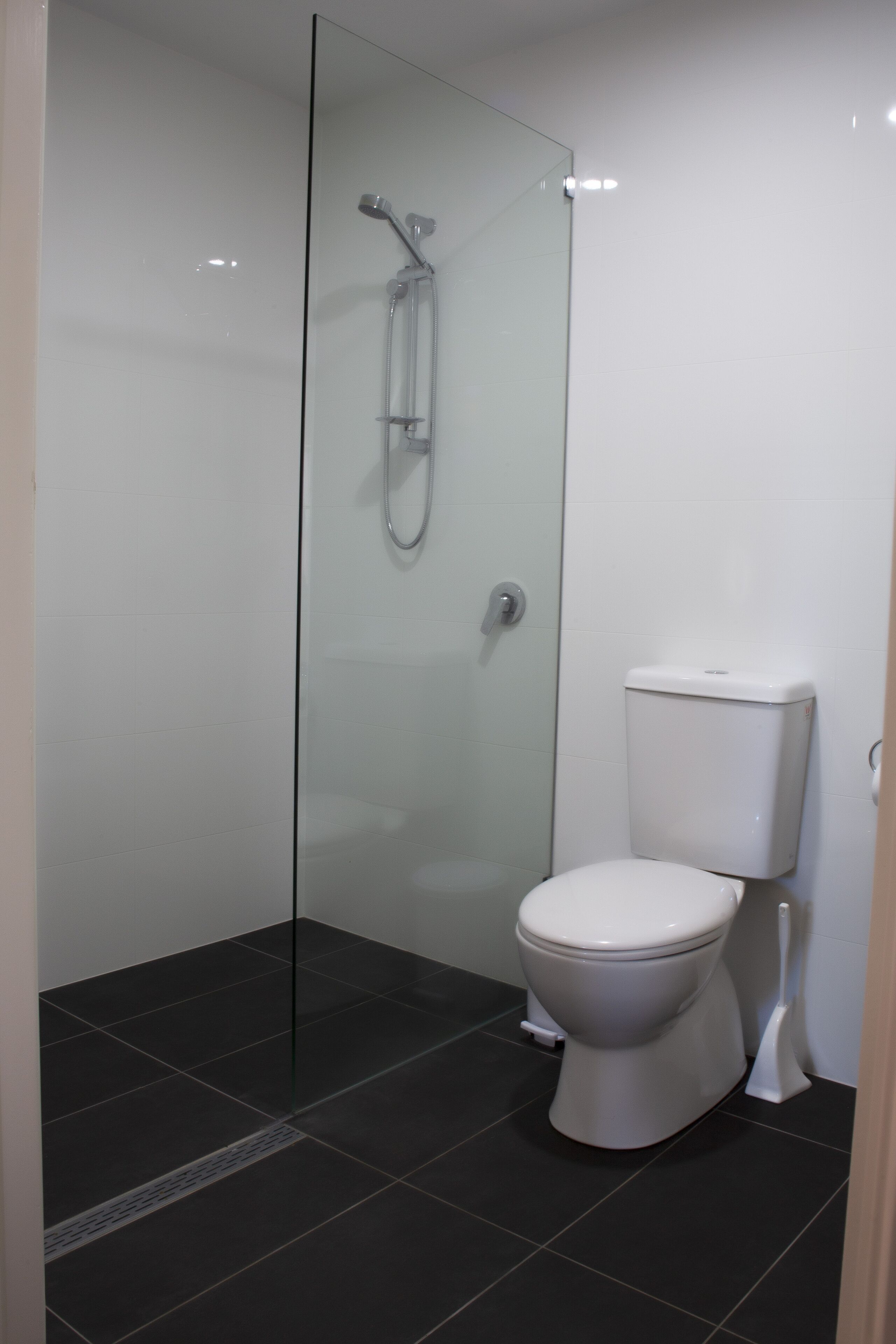 A modern bathroom with a glass-enclosed shower, a white toilet, and dark tiled flooring.