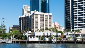 Hotel sul lungomare, dallo stile architettonico moderno, con un edificio in vetro ben visibile sullo sfondo, un pontile con una piccola imbarcazione e una passeggiata pedonale lungo l'acqua.