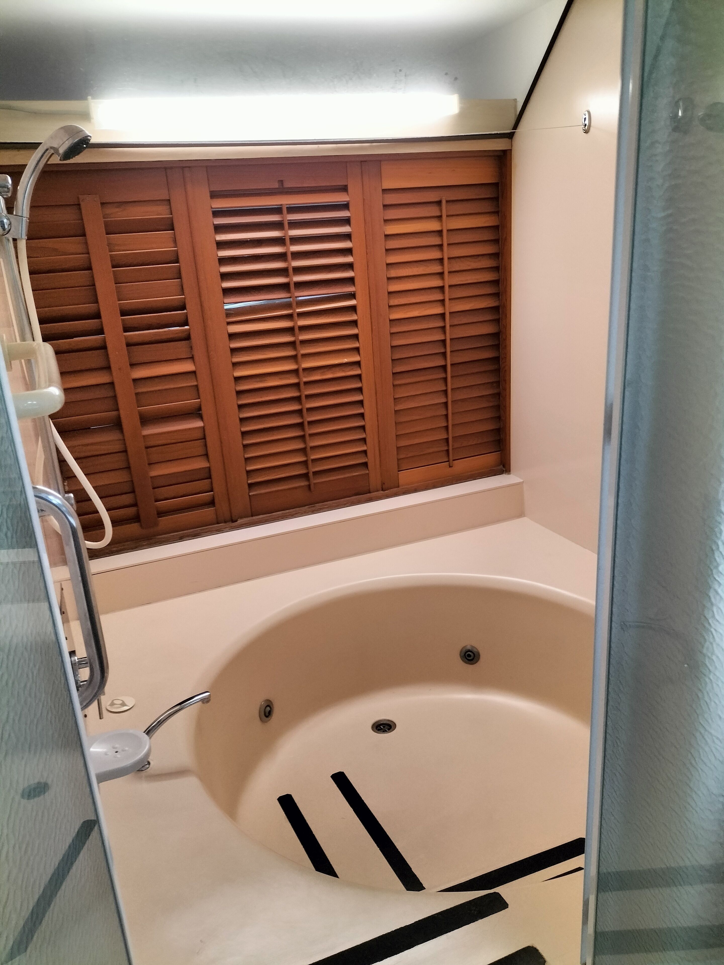 A bathroom with a bathtub, wooden blinds, and a shower area.