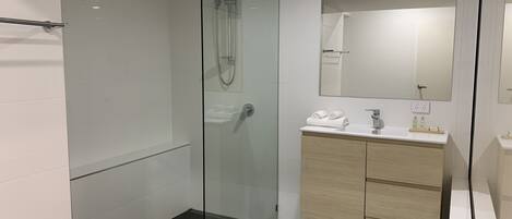 Un baño moderno con ducha envuelta en vidrio, un lavabo blanco con espejo y un mueble de tocador de madera.