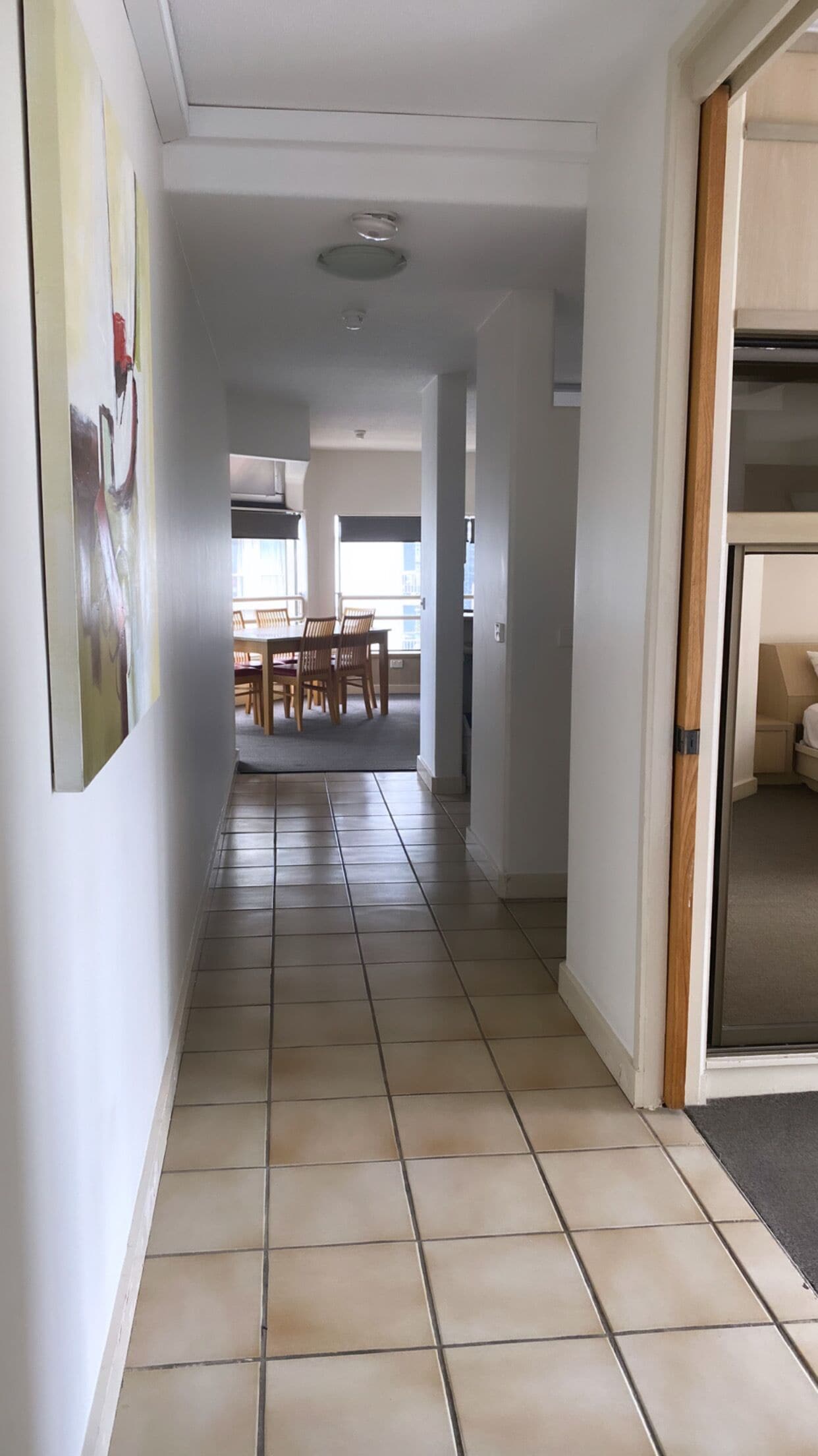 A hallway with tiled flooring leading to a dining area with a table and chairs.