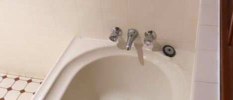 A bathroom with a white bathtub, a single faucet, and a drain. The floor has a hexagonal tile pattern.
