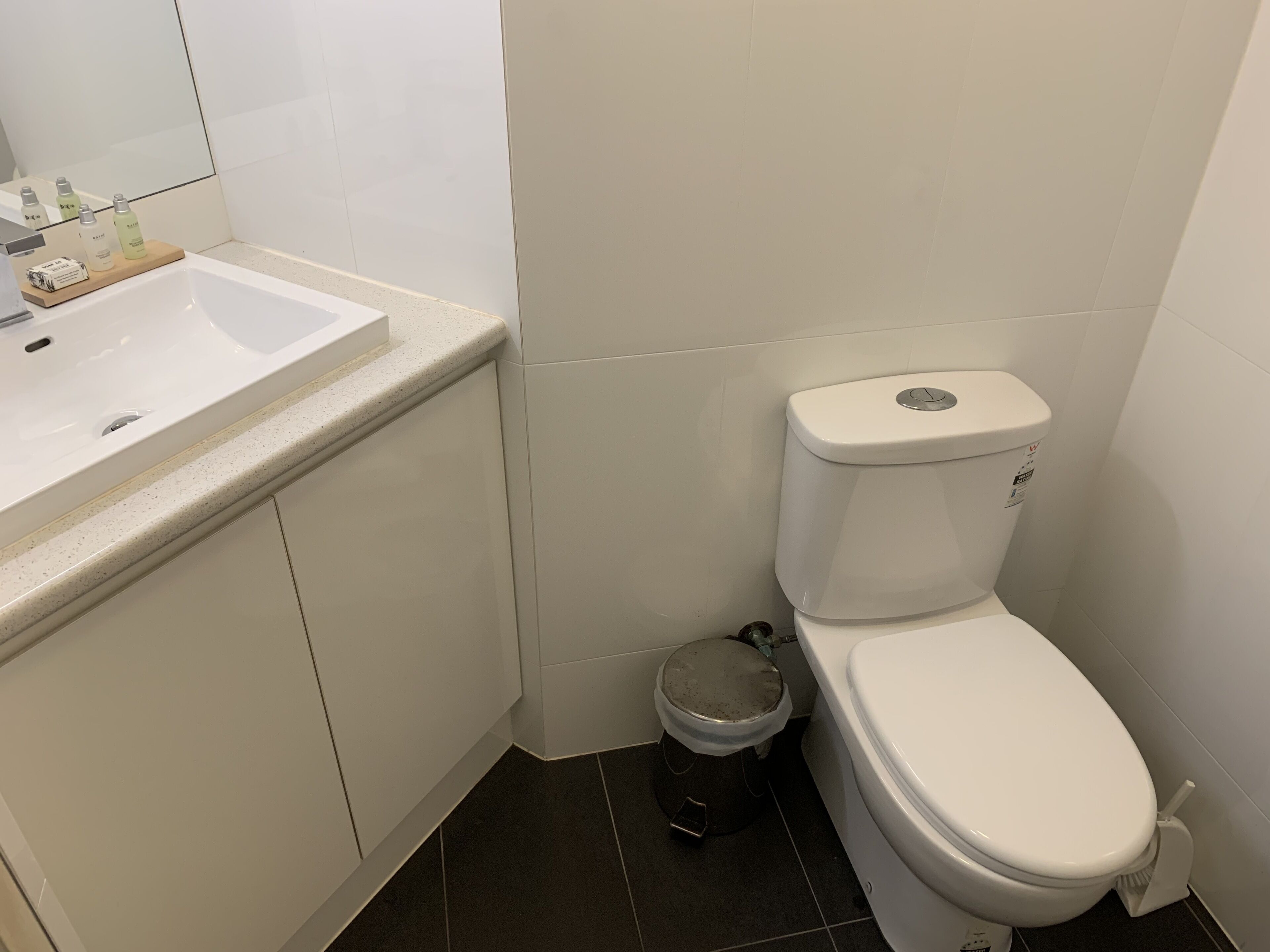 A small bathroom with a white sink, toilet, and trash can.