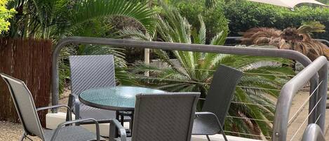 Un'area patio con un tavolo rotondo e quattro sedie, circondata da una recinzione in metallo e diverse piante.