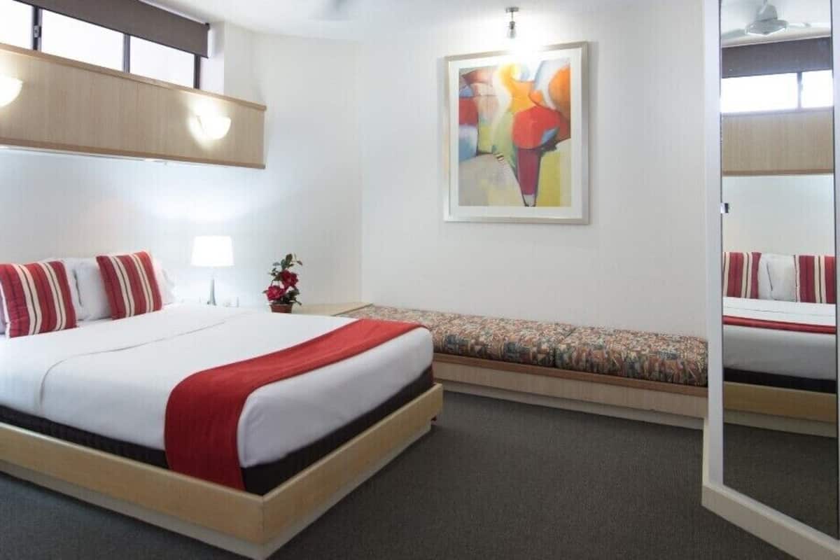 Una habitación de hotel moderna con cama, mesitas de noche, un banco, un cuadro y un armario.