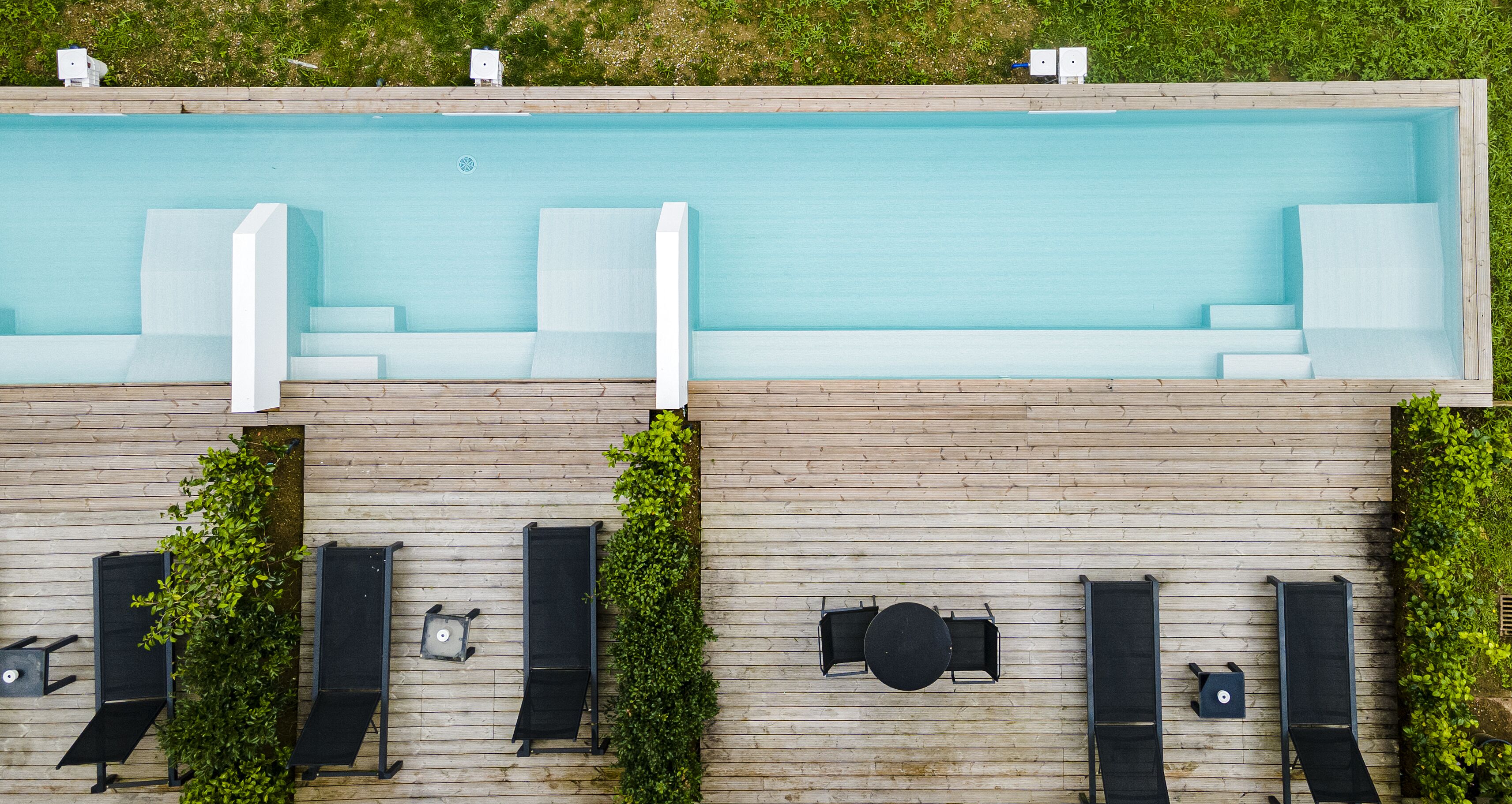 A rooftop pool with a wooden deck, lounge chairs, and a table.