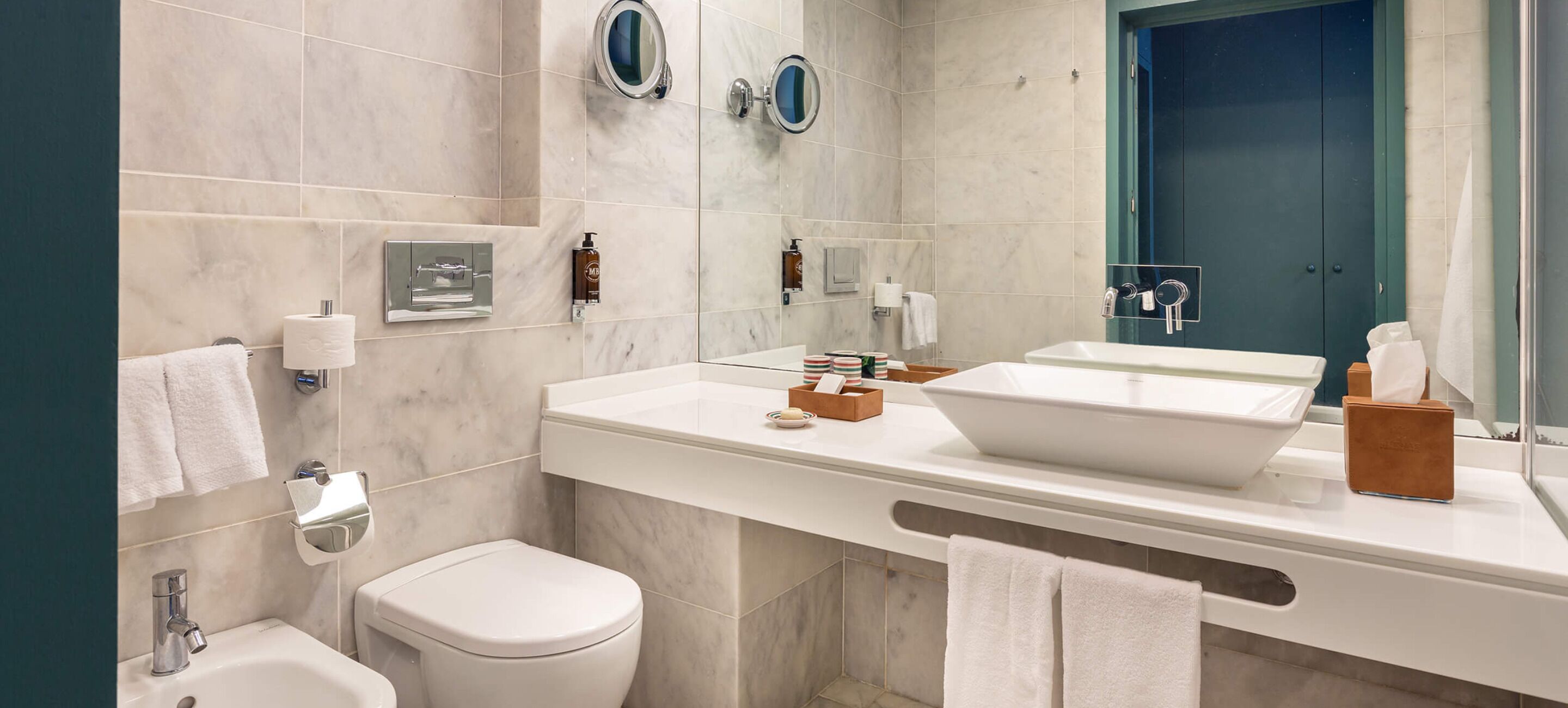 Un baño moderno con un lavamanos blanco, un espejo, un inodoro y una zona de ducha.