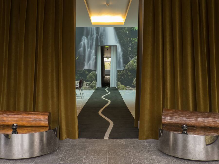 A hotel lobby with a waterfall mural, a reception desk, and a path leading to the entrance.