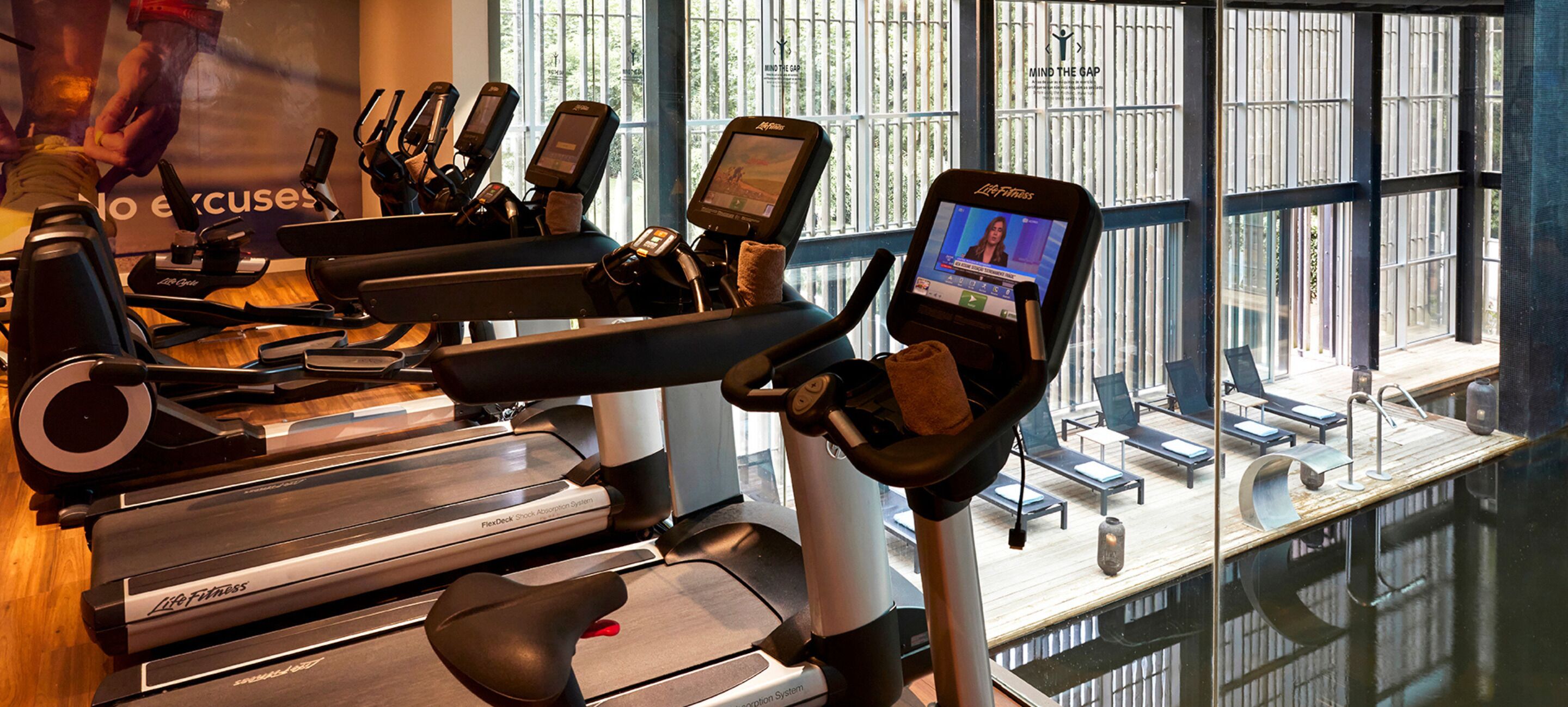 A gym with multiple cardio machines, including treadmills and an elliptical, with a large window in the background.