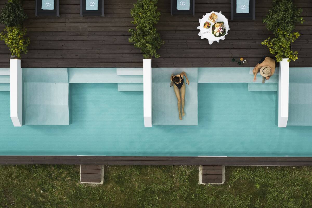 Vista aérea de un área de piscina en la azotea con tres macetas blancas, una mesa de comedor con comida y dos personas relajándose.