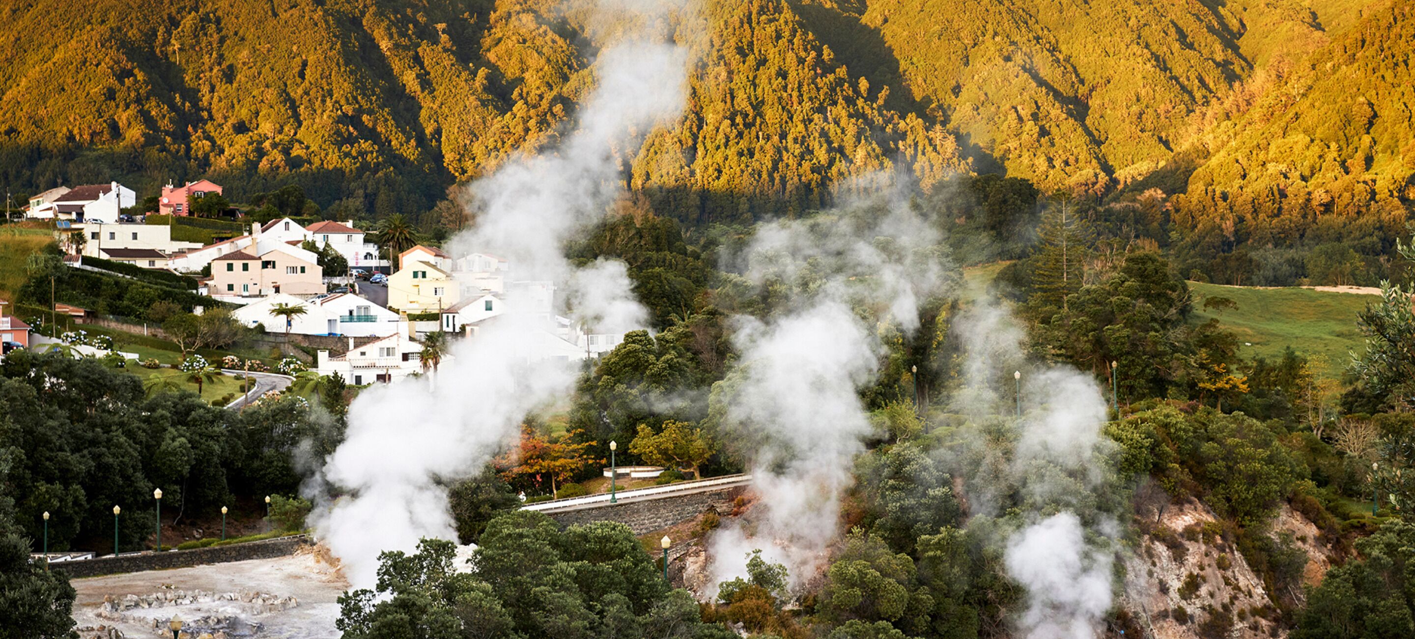 A mountainous landscape with a small village, steam rising from a central structure, and a railway track.