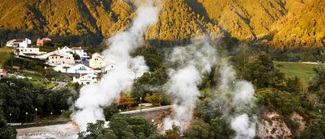 A mountainous landscape with a small village, steam rising from a central structure, and a railway track.