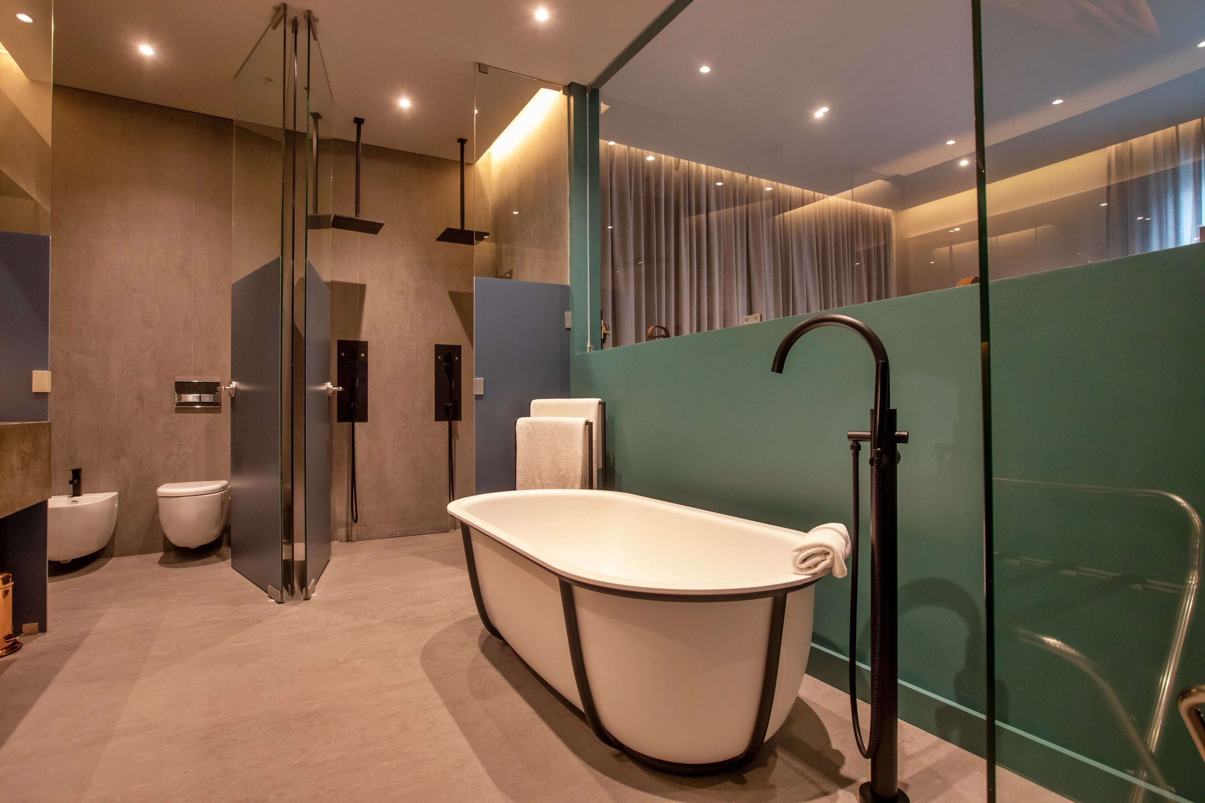 Een moderne badkamer met een vrijstaand bad, een douchecabine van glas en een glazen scheidingswand.