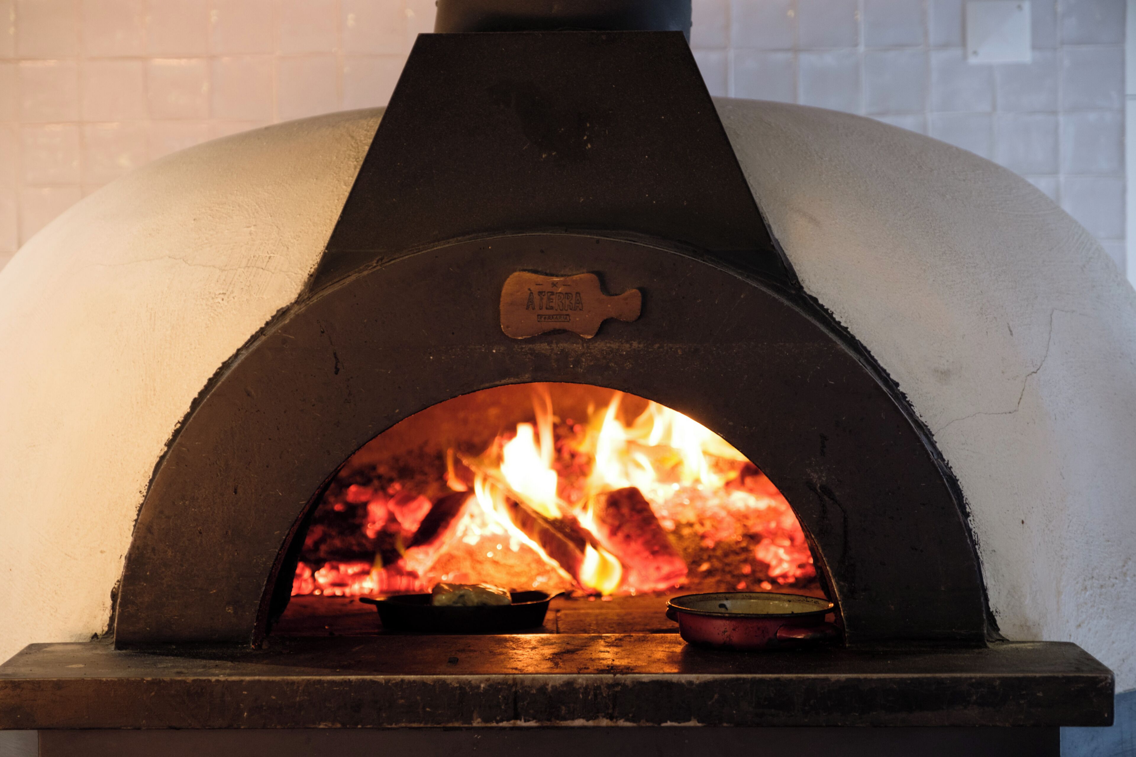 Een pizzaoven met bakstenen en een vuur, een pizzaspade en een pizzasteen op het aanrecht.