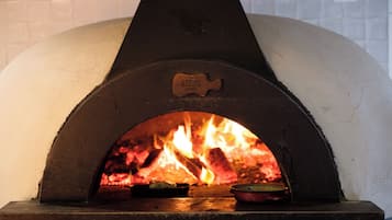 Een pizzaoven met bakstenen en een vuur, een pizzaspade en een pizzasteen op het aanrecht.
