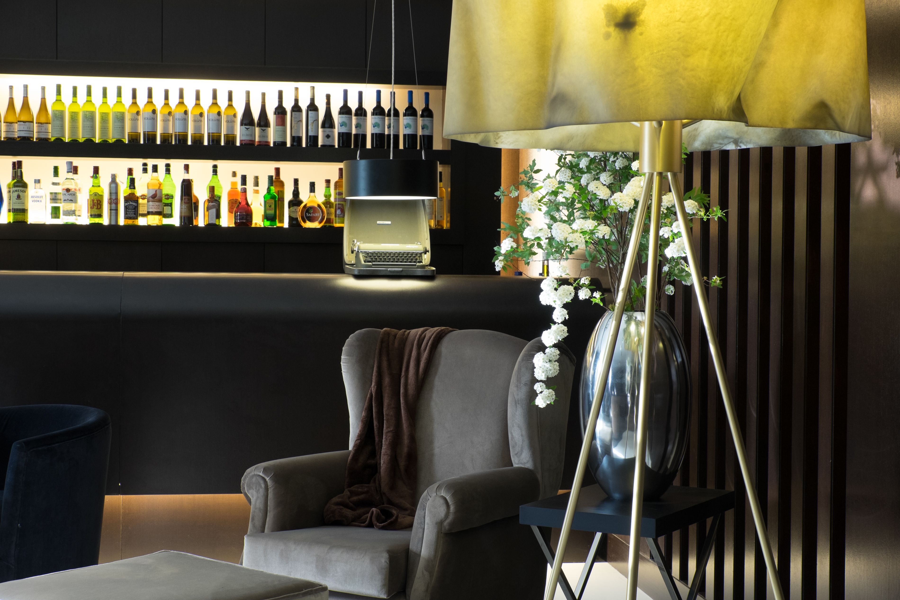 Uma área de bar com diversos frascos, uma máquina de café, uma cadeira e um vaso decorativo com flores.