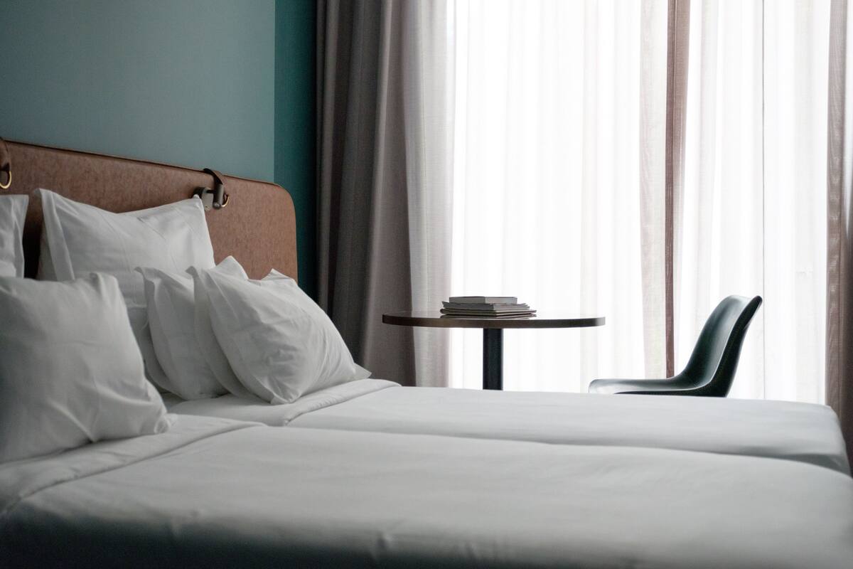 Habitación de hotel con una cama, una mesita redonda con libros y una silla.