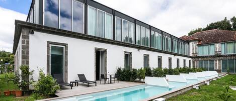 Un edificio moderno con piscina, sillones de descanso y jardín.