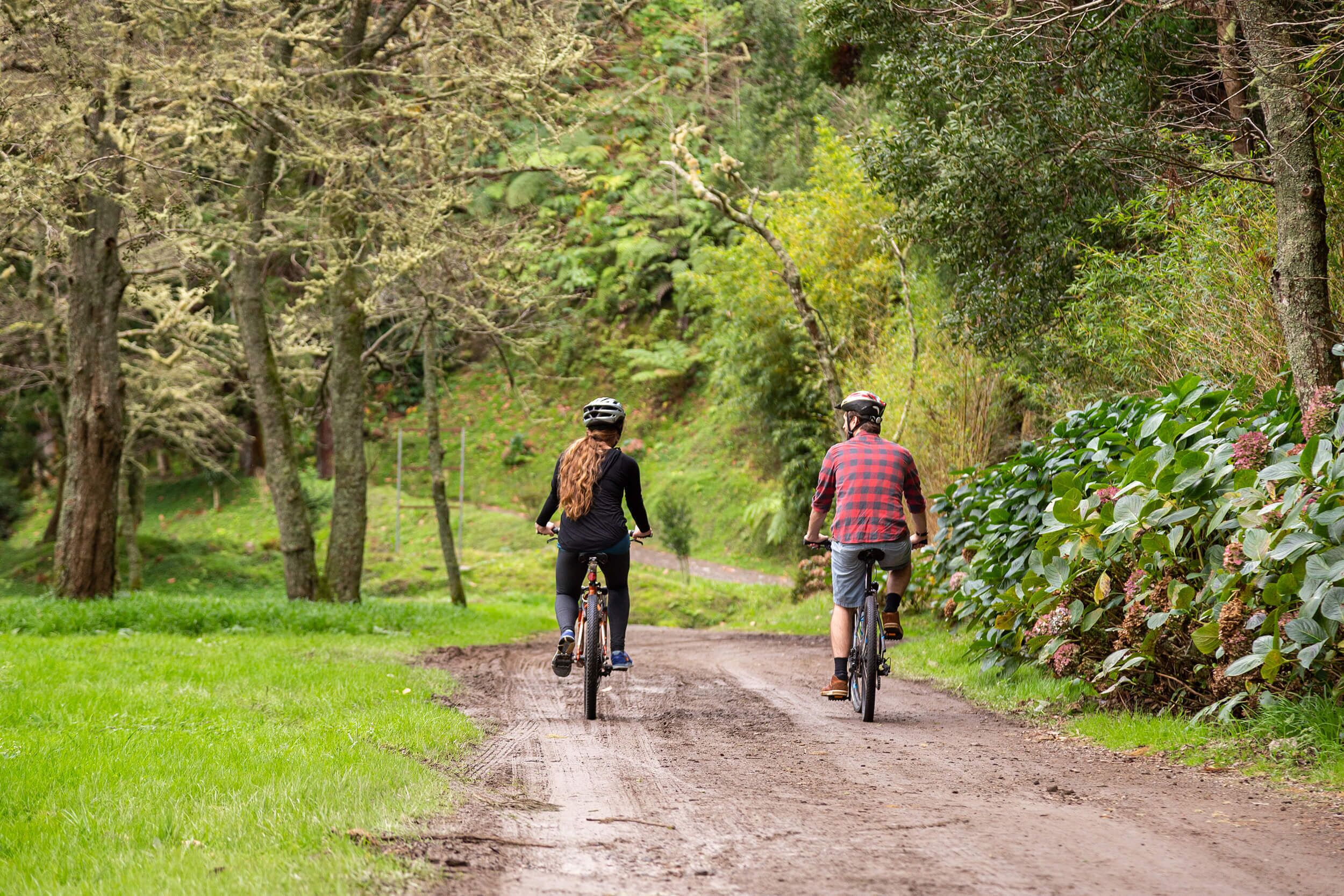 Dos personas montando en bicicleta por un sendero de tierra rodeado de árboles y vegetación.