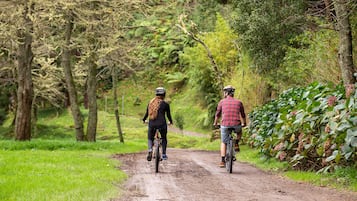 Dos personas montando en bicicleta por un sendero de tierra rodeado de árboles y vegetación.