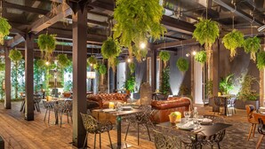 Un espacio interior amplio con plantas colgantes, suelo de madera, asientos de cuero y mobiliario moderno.