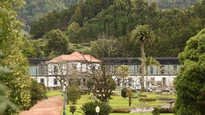 Un edificio blanco con tejado rojo, rodeado de vegetación exuberante y un promontorio boscoso.