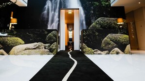 Un vestíbulo de hotel con un mural grande de una cascada, una alfombra negra que conduce a la entrada, e iluminación moderna.