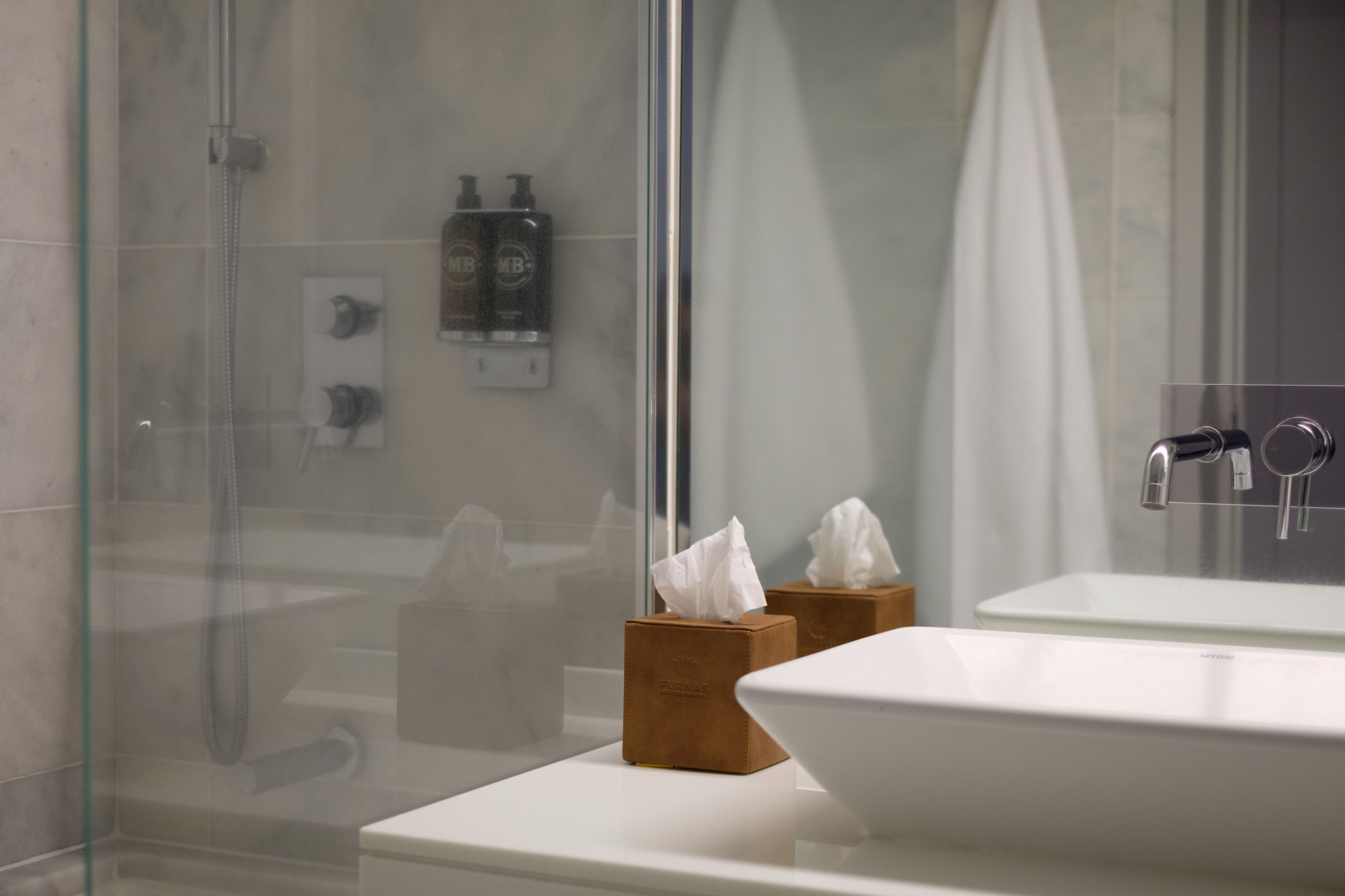 A bathroom with a glass shower enclosure, a white sink, and two wooden tissue boxes.